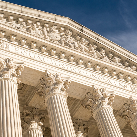 Low-angle view of the U.S. Supreme Court building's marble facade, featuring Corinthian columns and the engraved motto