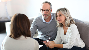 Gemini said A senior couple sitting on a sofa, looking intently and listening to a woman who is seen from behind during a professional consultation.
